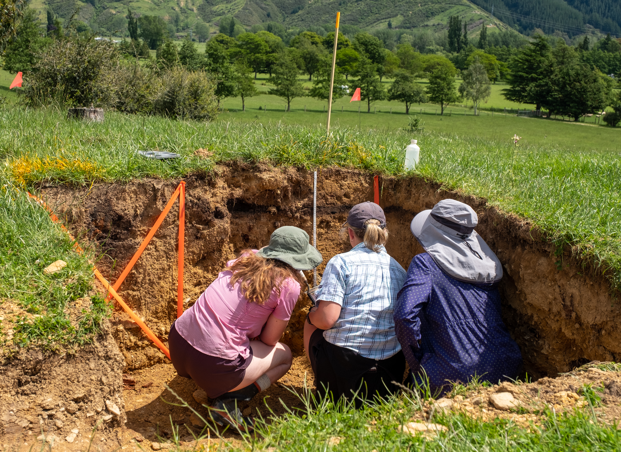 Three people looking at soil in a square hole